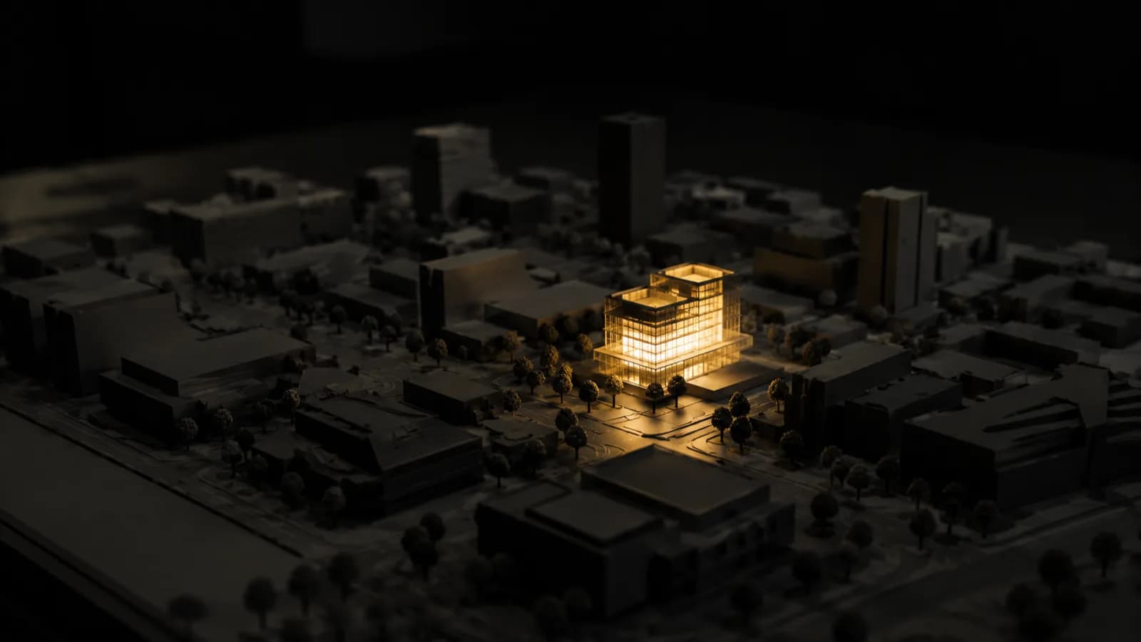 A dark architectural model of a city block, one building lit from within by warm gold light